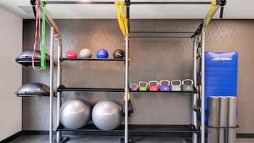 Una sbarra per trazioni con elastici di resistenza, kettlebell, palle mediche e un tappetino blu per esercizi.