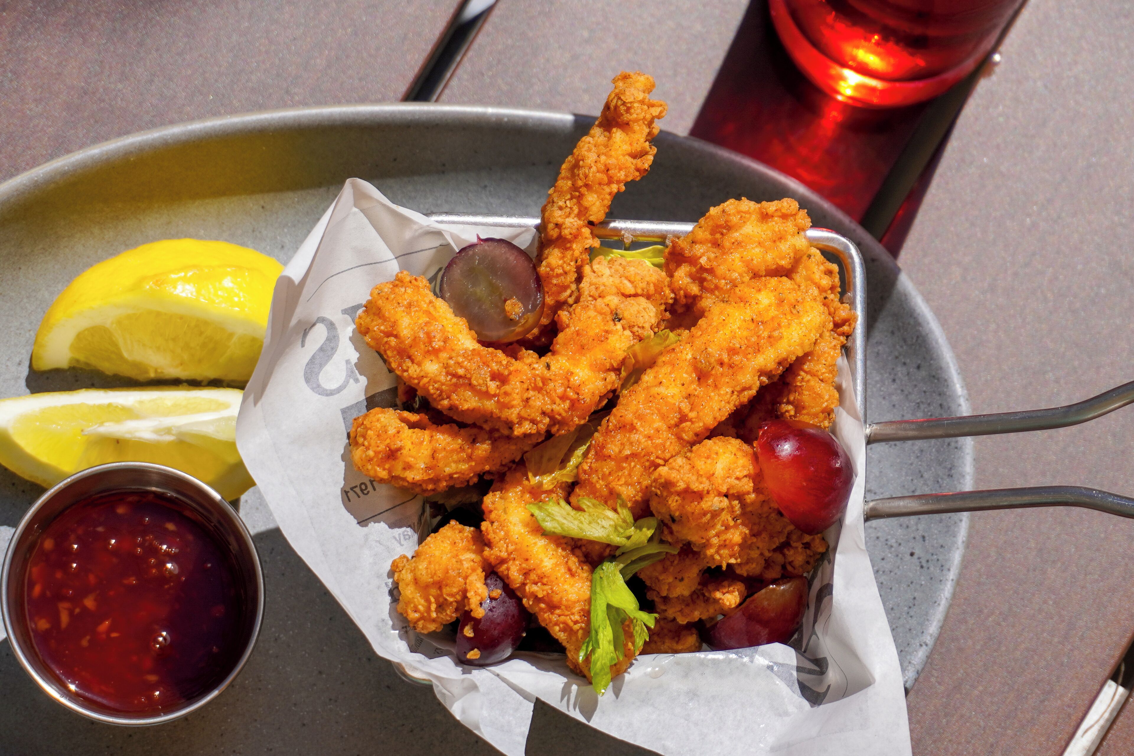 Un plato de pollo frito con gajos de limón y un recipiente pequeño de salsa.