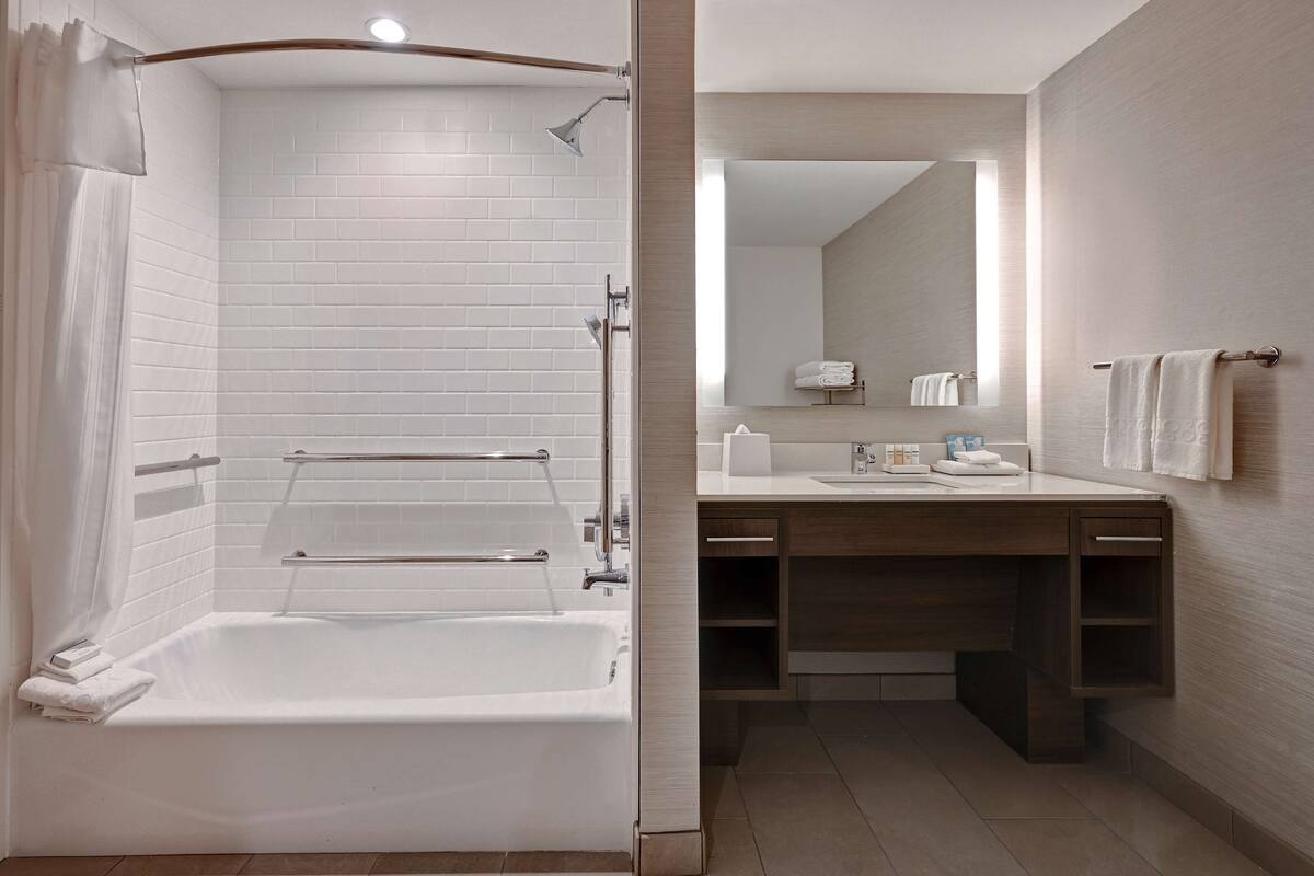 A modern bathroom with a walk-in shower, a bathtub, a vanity with a mirror, and a towel rack.