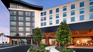A modern hotel with a curved facade, large windows, and a landscaped entrance with trees and plants. - Home2Suites by Hilton Anaheim Resort (Anaheim)