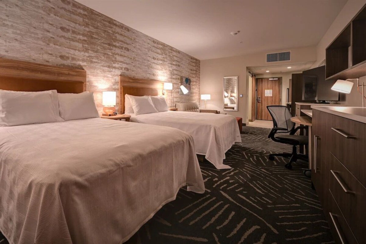 A hotel room with two beds, a desk, a chair, and a television.