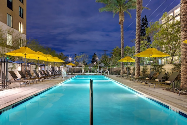 Una piscina al aire libre, sombrillas, sillones reclinables de piscina