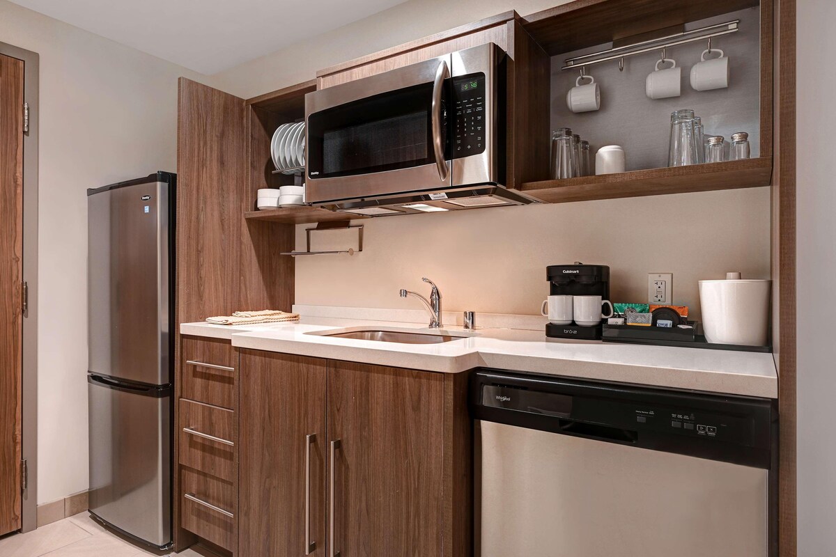 A modern kitchen with stainless steel appliances, wooden cabinets, a built-in microwave, and a coffee maker.