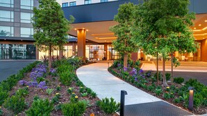 A modern hotel entrance with a curved pathway, landscaped garden, and trees. - Home2Suites by Hilton Anaheim Resort (Anaheim)