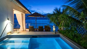 A swimming pool with a view of the ocean, a covered seating area with chairs, and a palm tree. - The Sandpiper (Holetown)