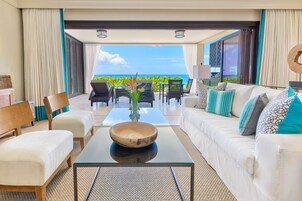 Un moderno salón con una mesa de centro de vidrio, un sofá blanco y sillones, con vistas a un paisaje marino.
