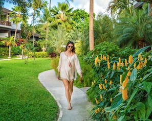 A woman walking on a concrete path surrounded by lush greenery and palm trees.