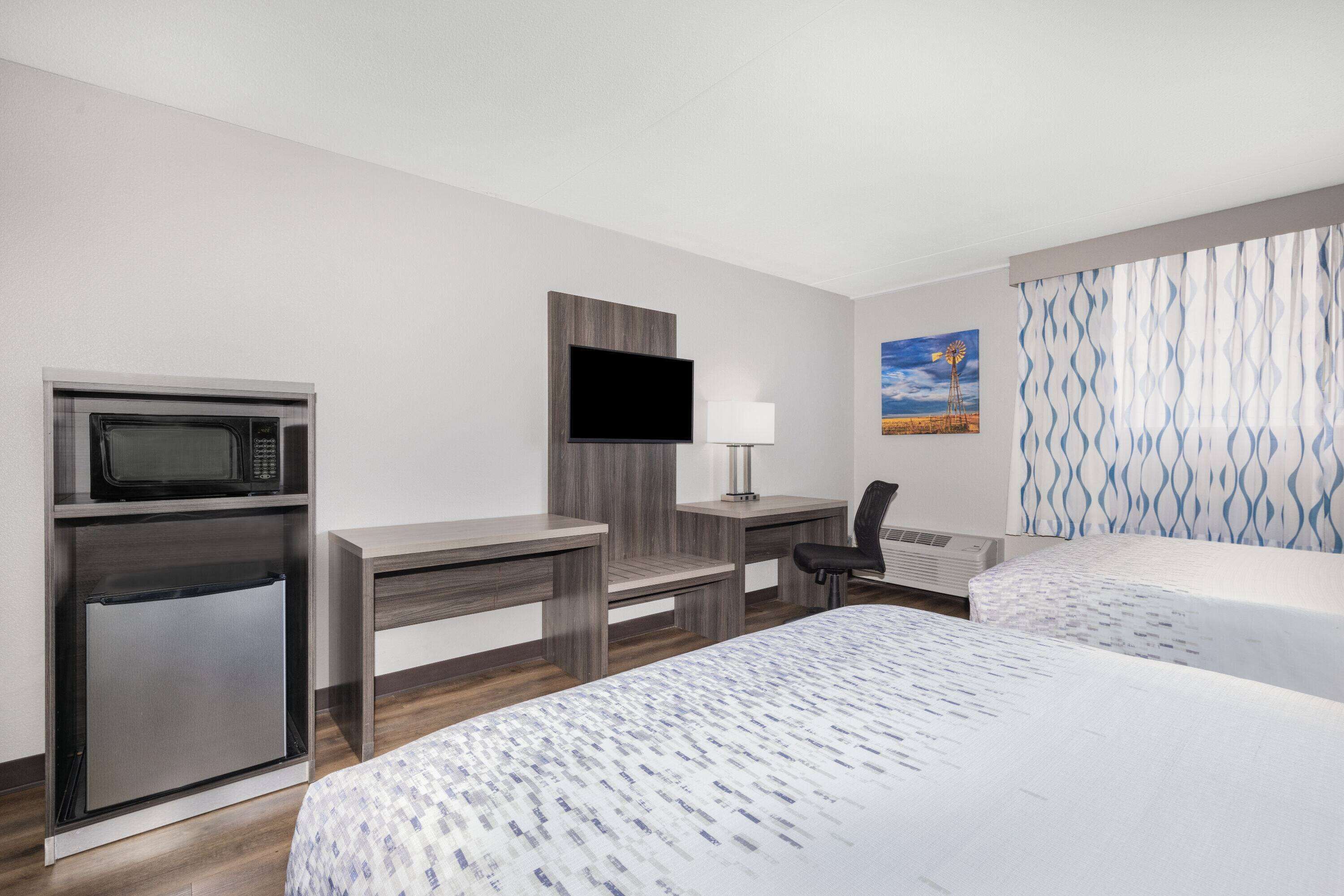 Een hotelkamer met een bed, een bureau met een flatscreen-televisie, een magnetron, een koelkast en een raam met gordijnen met een patroon.
