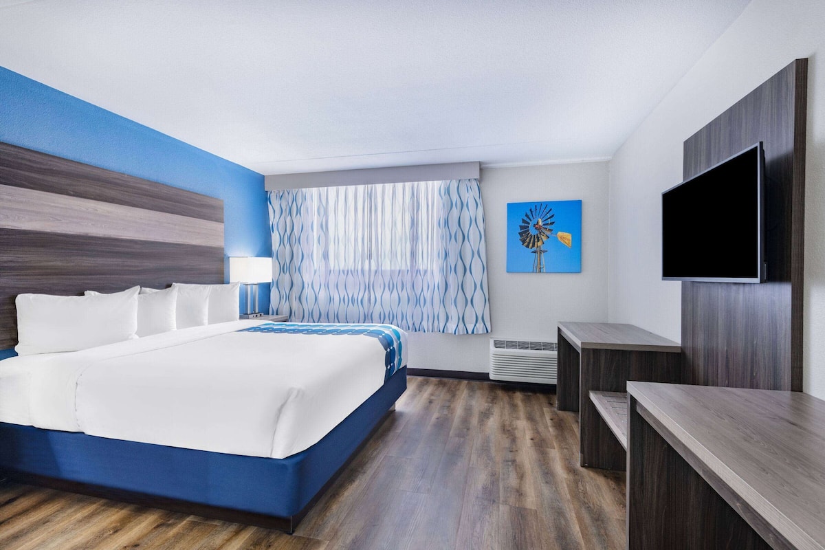 A hotel room with a large bed, a flat-screen TV, a desk, and a window with curtains.