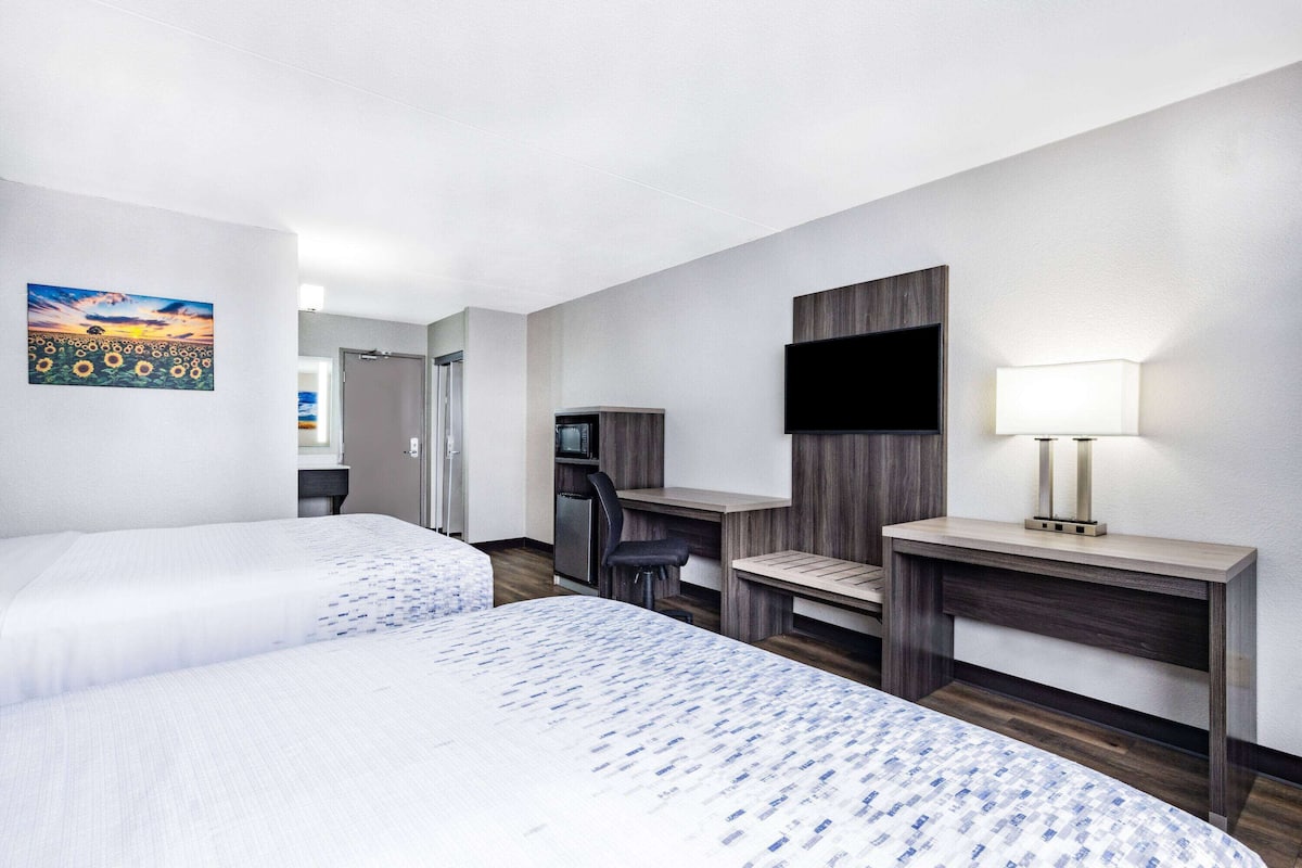 A hotel room with two beds, a desk with a TV, a desk lamp, and a painting on the wall.