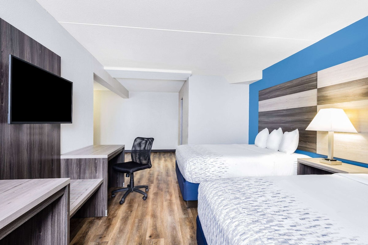 A hotel room with a desk, two beds, a TV, and a lamp.