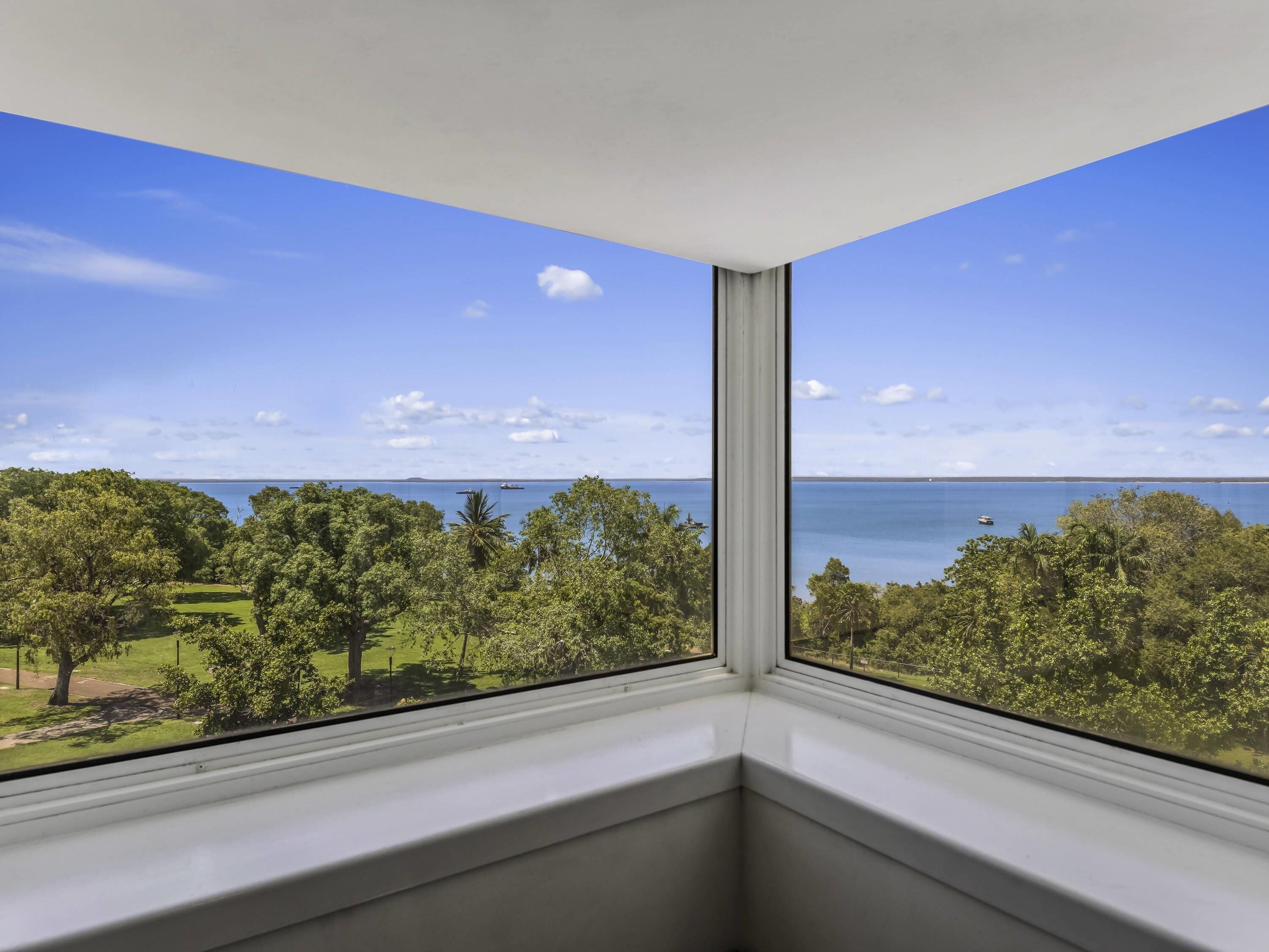 Rincón de una habitación con vista a un cuerpo de agua, árboles y cielo despejado.