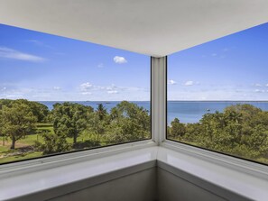 A corner of a room with a view of a body of water, trees, and a clear sky.
