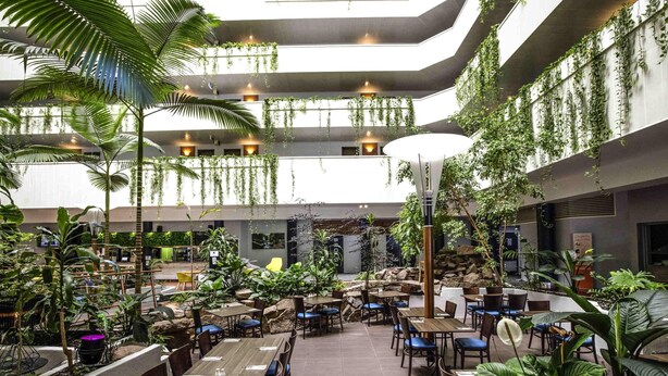 A multi-level indoor space with tables and chairs, surrounded by various plants and greenery. - Novotel Darwin CBD (Darwin)