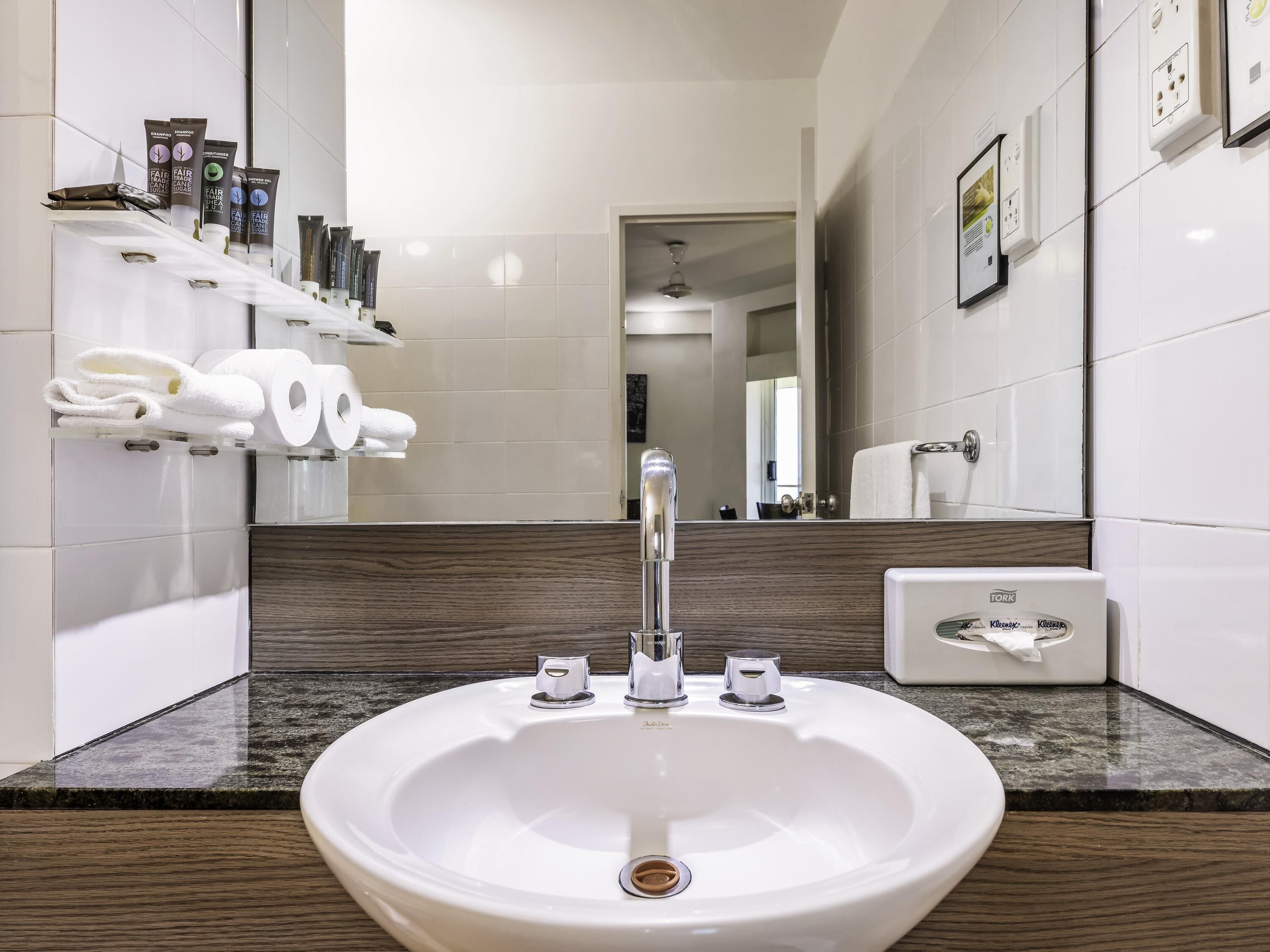 A modern bathroom with a white sink, a mirror, and toiletries on shelves.