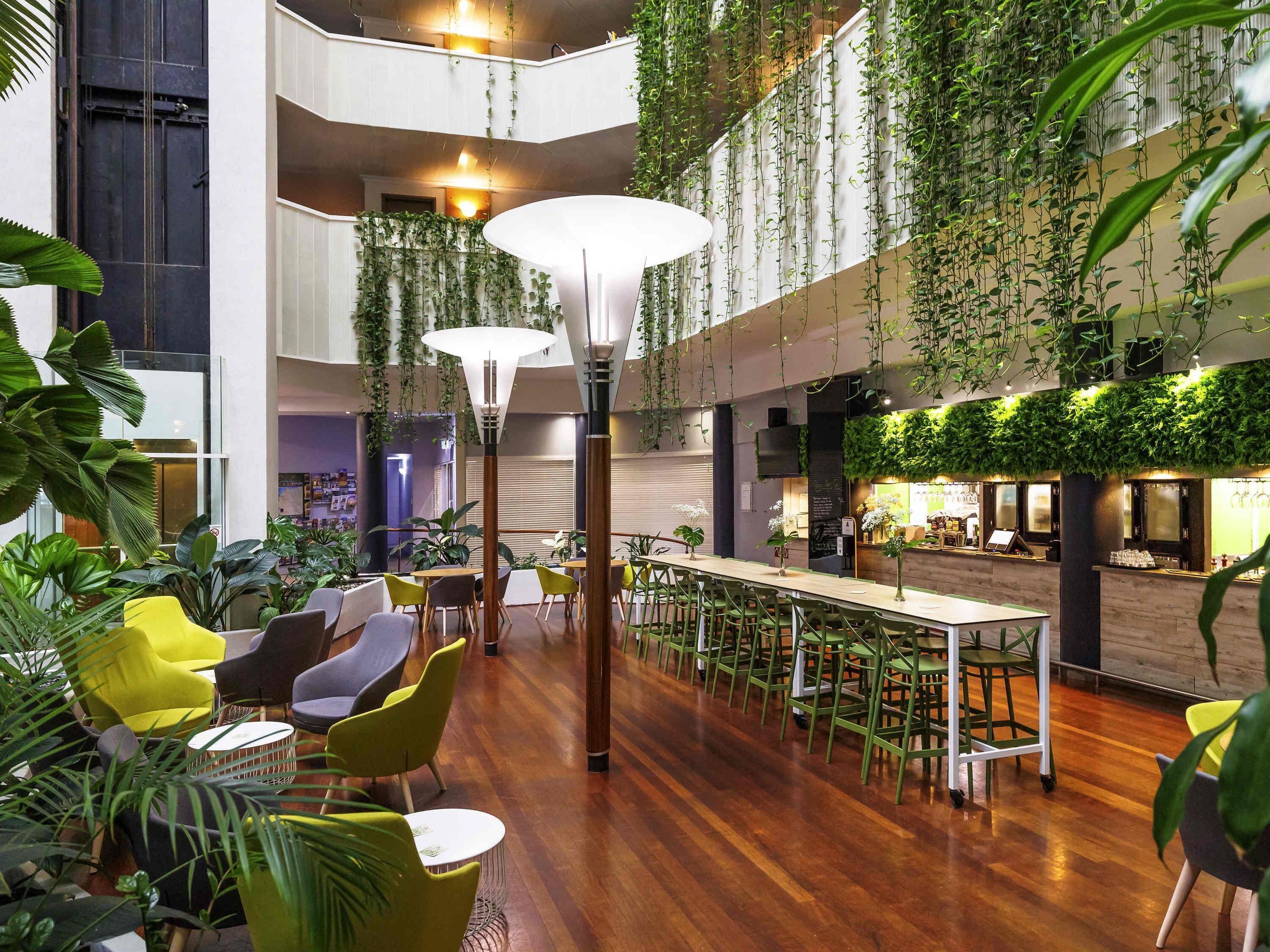 A spacious indoor area with a long dining table, multiple chairs, and hanging plants.