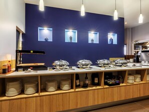 A buffet setup with labeled food items, a coffee machine, and a wine bottle.