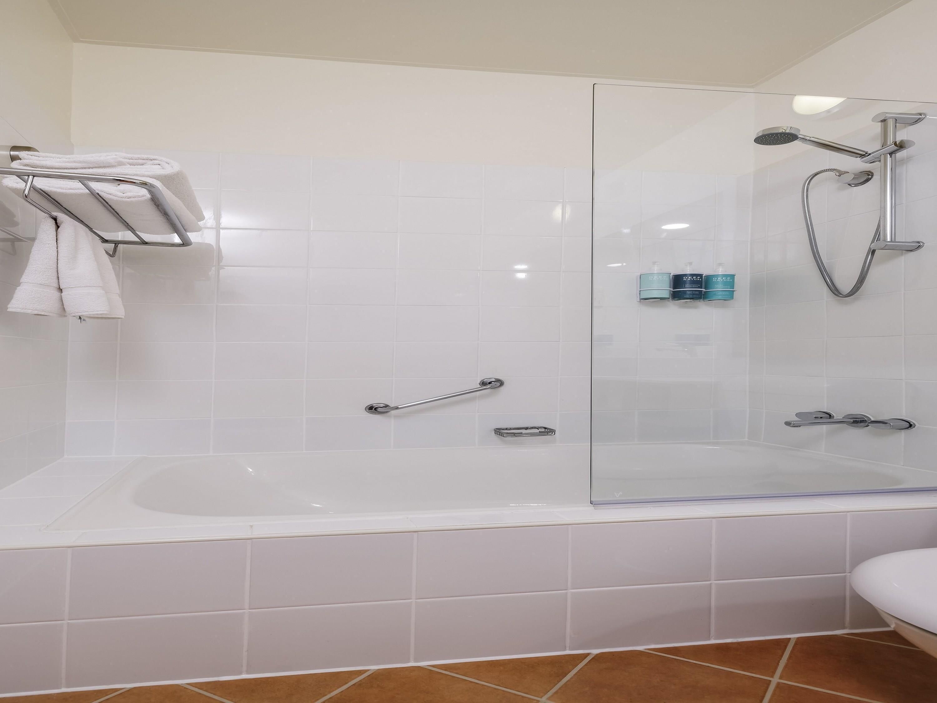 A modern bathroom with a glass-enclosed shower, a white bathtub, and a towel rack.