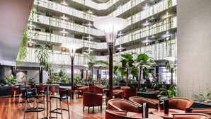 A spacious indoor area with multiple seating arrangements, including red chairs and tables, surrounded by various plants and greenery. - Novotel Darwin CBD (Darwin)