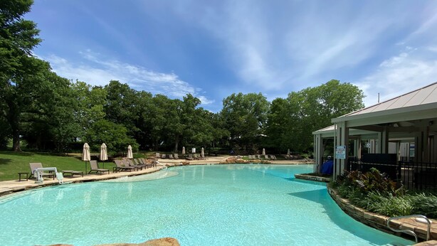 A clear swimming pool with lounge chairs and umbrellas, surrounded by trees and a covered pavilion. - Sheraton Arlington (Arlington)