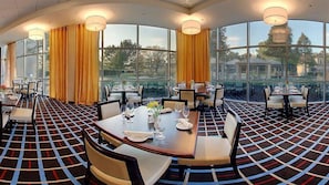 A restaurant with a checkered floor pattern, large windows with yellow curtains, and multiple dining tables set for guests. - Sheraton Arlington (Arlington)