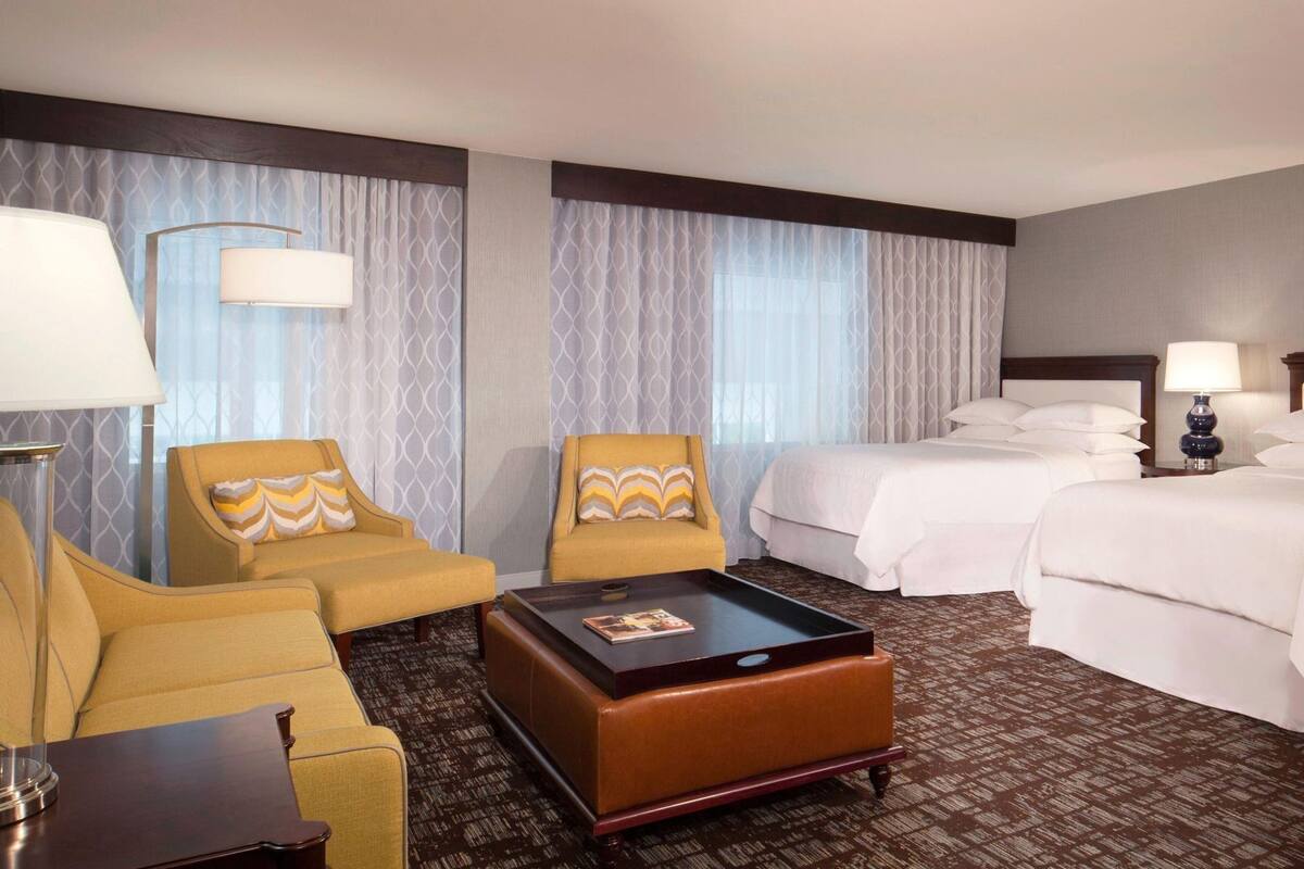 A hotel room with two single beds, a sofa, a coffee table, and a lamp.