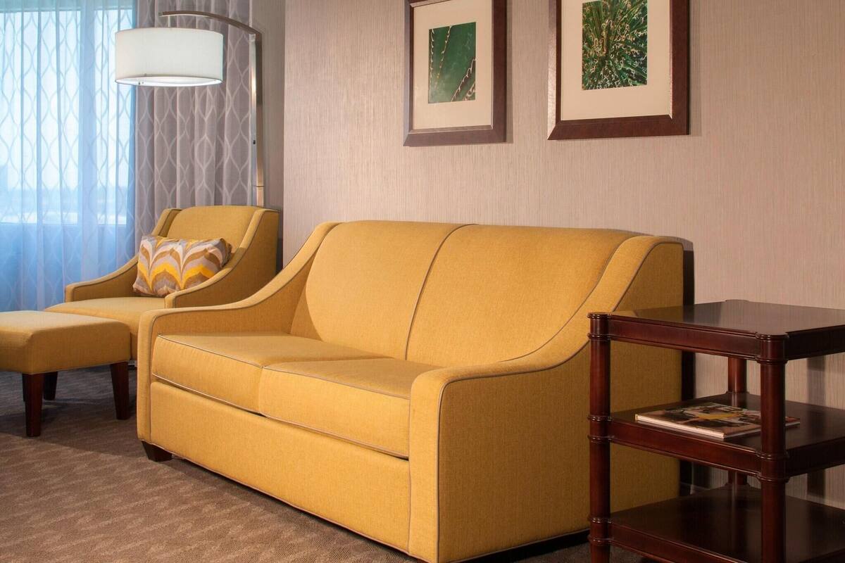 A yellow sofa with a matching ottoman, a wooden side table, and two framed pictures on the wall.