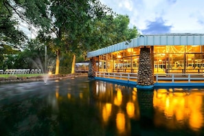 A building with a glass facade, stone pillars, and a reflection in the water. - Sheraton Arlington (Arlington)
