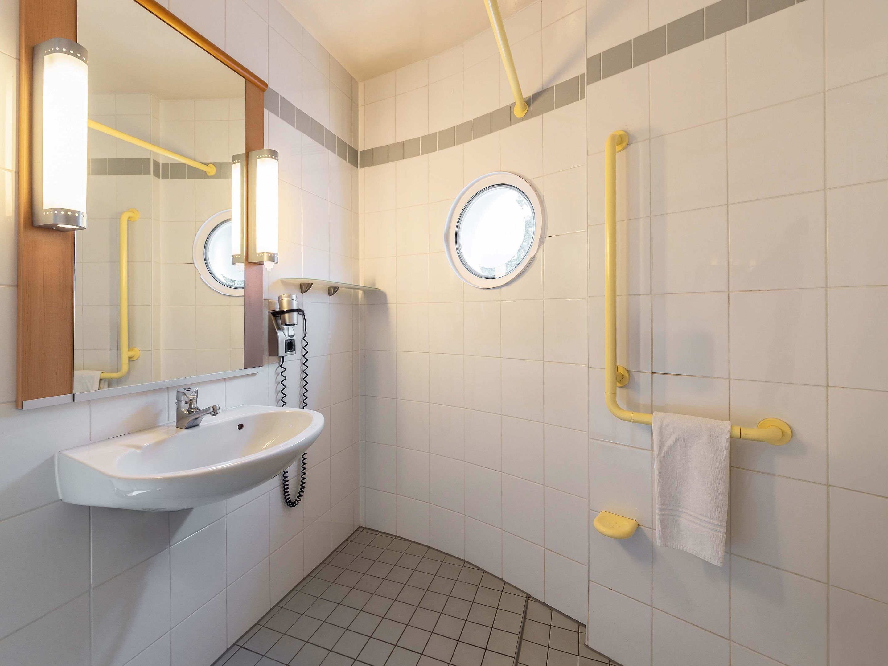 Ein modernes Badezimmer mit Waschbecken, Spiegel und zwei Haltegriffen.