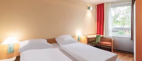 Habitación de hotel con dos camas, un escritorio, una silla y una ventana con cortinas.