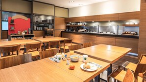 A modern restaurant with wooden tables and chairs, a counter with kitchen appliances, and a red accent wall.