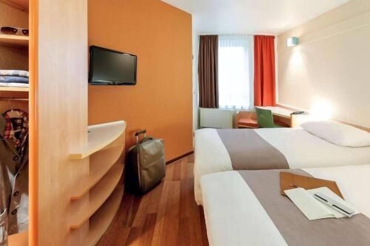 A hotel room with two beds, a TV, a desk, and a wardrobe.