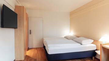 A compact hotel room with a bed, a TV mounted on the wall, and a wooden floor.