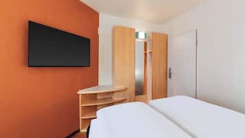 Ein Hotelzimmer mit einem Bett, einem an der Wand montierten Fernseher, einem Holzschrank und einem kleinen Regal.