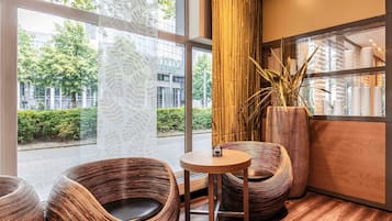 Ein modernes Interieur mit großen Fenstern, Korbstühlen, einem runden Tisch und einer hohen Bambuspflanze.
