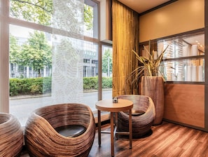 Un interior moderno con ventanas amplias, sillas de mimbre, una mesa redonda y una alta planta de bambú.