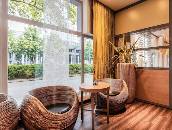 A modern interior with large windows, wicker chairs, a round table, and a tall bamboo plant.