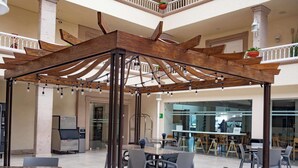 An indoor patio area with a wooden pergola, seating arrangements, and a bar area visible through the glass wall. - Best Western Plus Monterrey Colon (Monterrey)