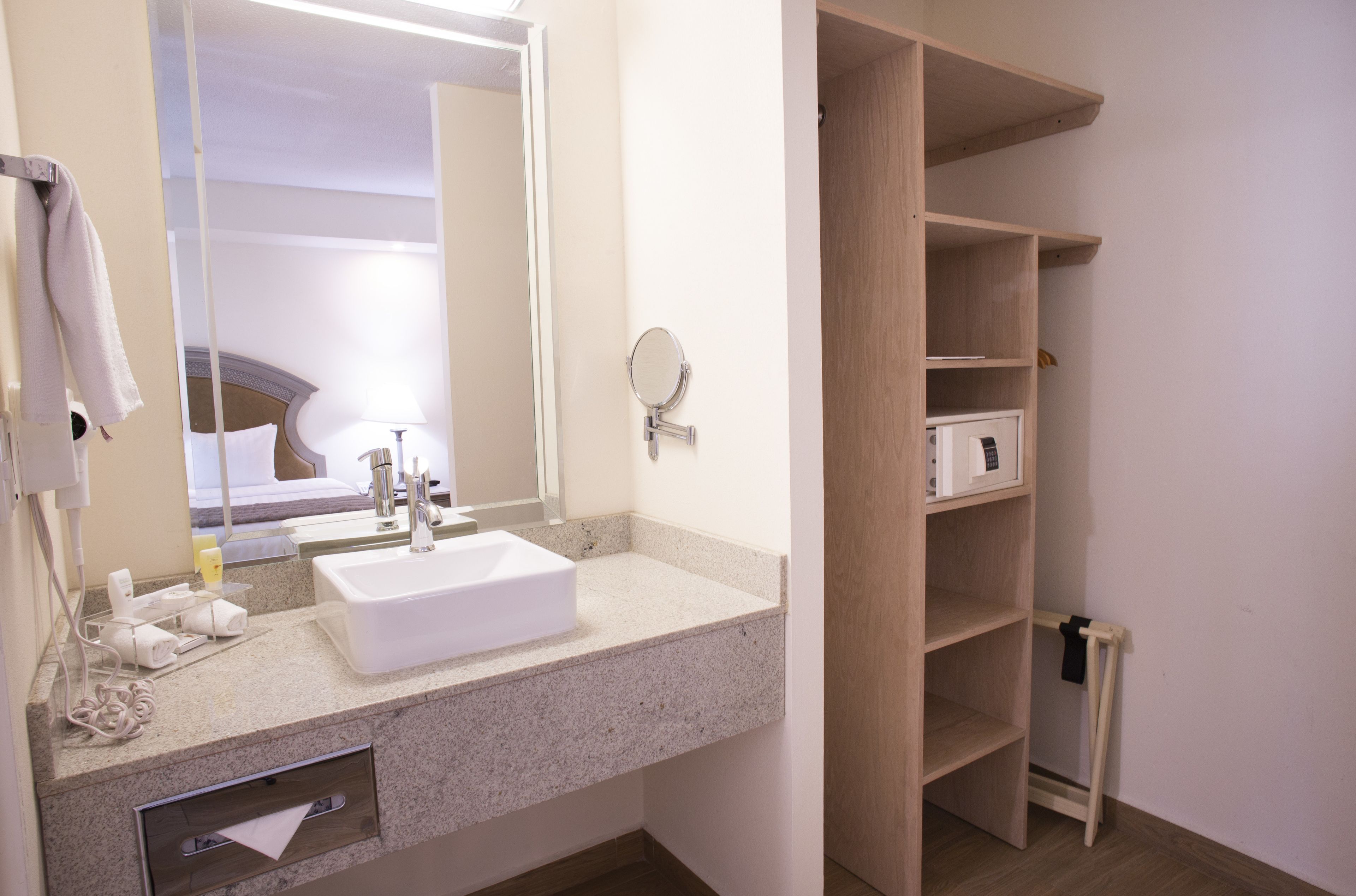 A hotel bathroom with a sink, mirror, and shelves.