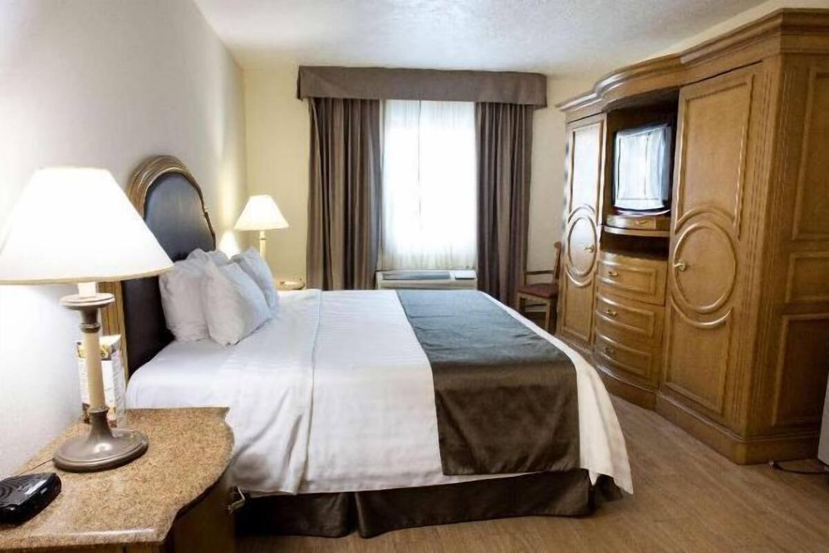 A hotel room with a bed, two bedside lamps, a desk with a telephone, and a wardrobe.