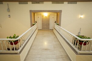 Un pasillo de hotel con piso de mármol, barandales blancos y plantas en macetas a ambos lados.