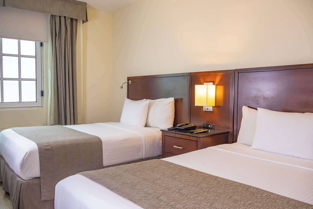 A hotel room with two beds, a nightstand with a phone, and a window with curtains.