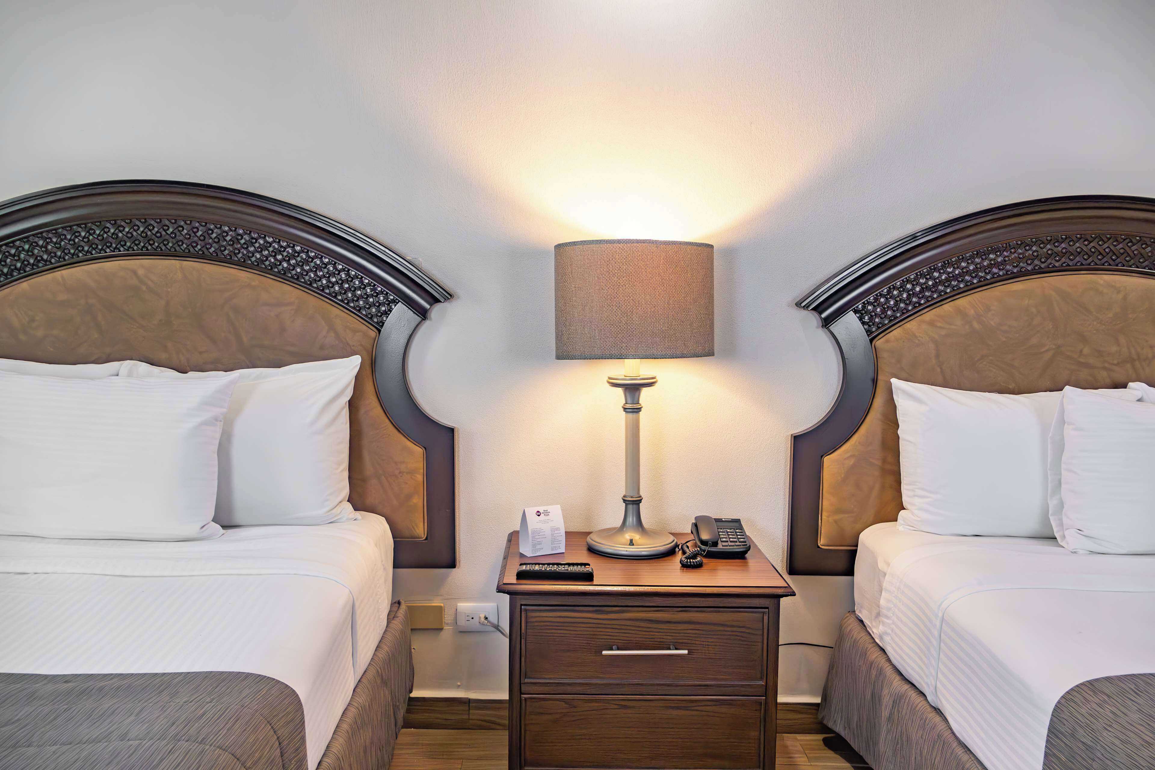 A hotel room with two beds, a nightstand with a lamp, a phone, and a small table.