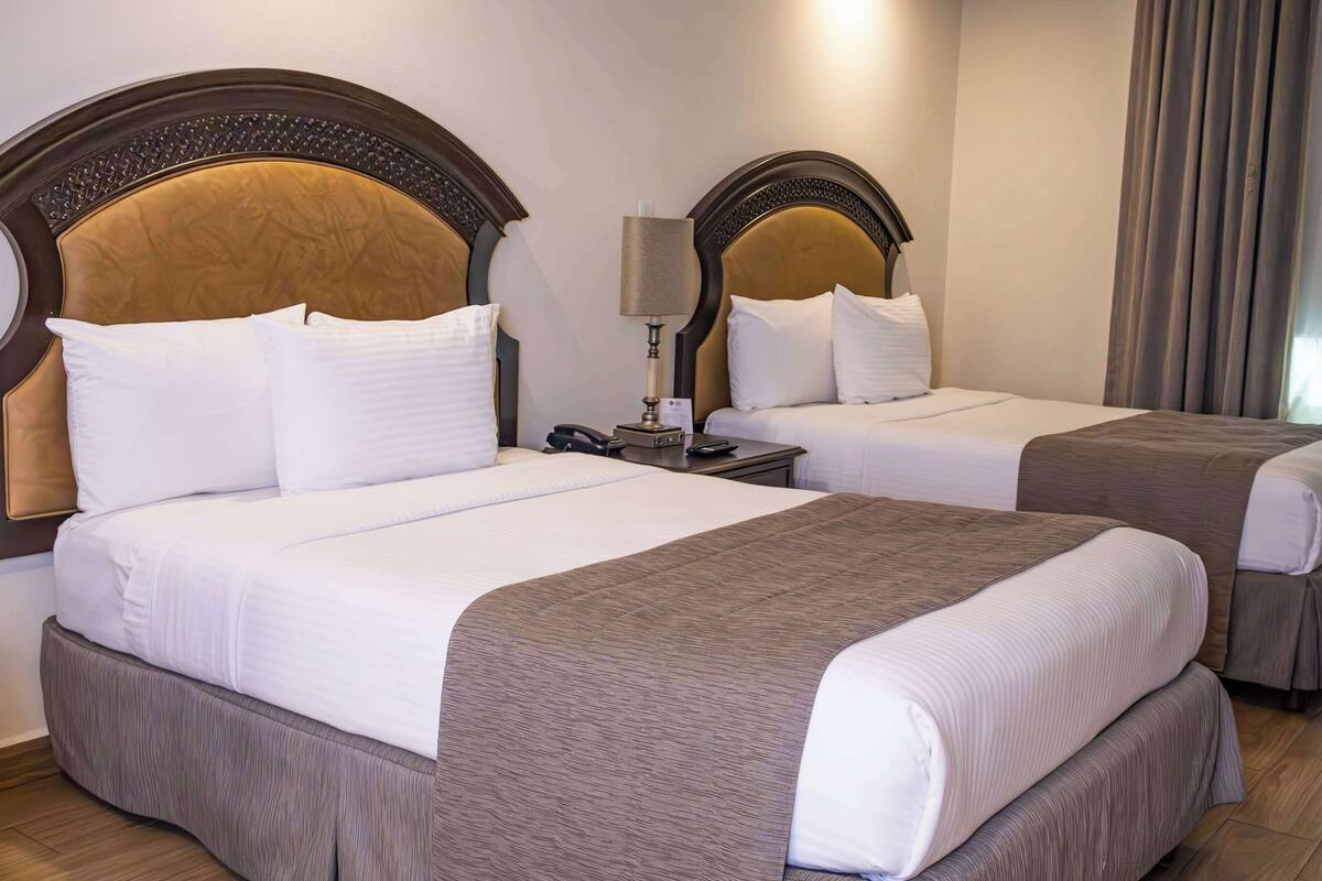 A hotel room with two beds, each with a headboard, a bedside table with a lamp, and a telephone.