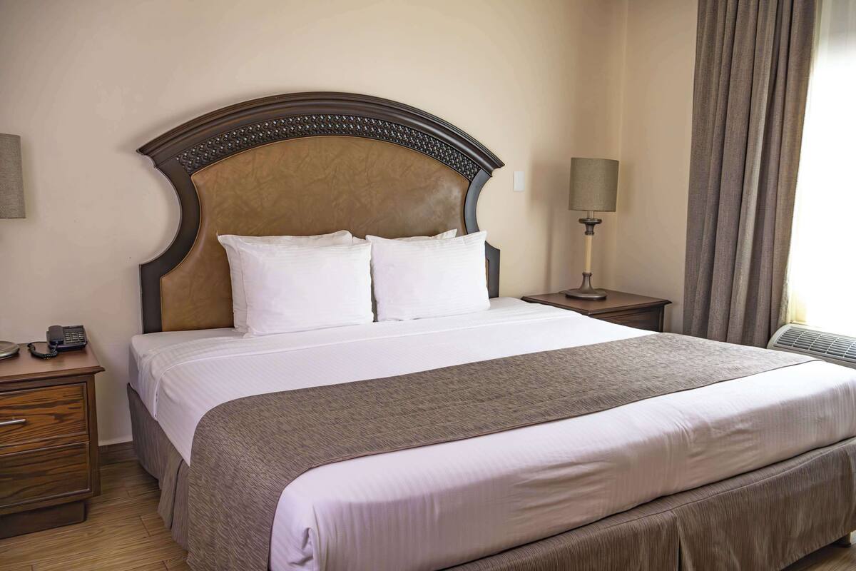 A neatly made bed with a wooden headboard, a bedside lamp, and a wooden nightstand with a telephone.