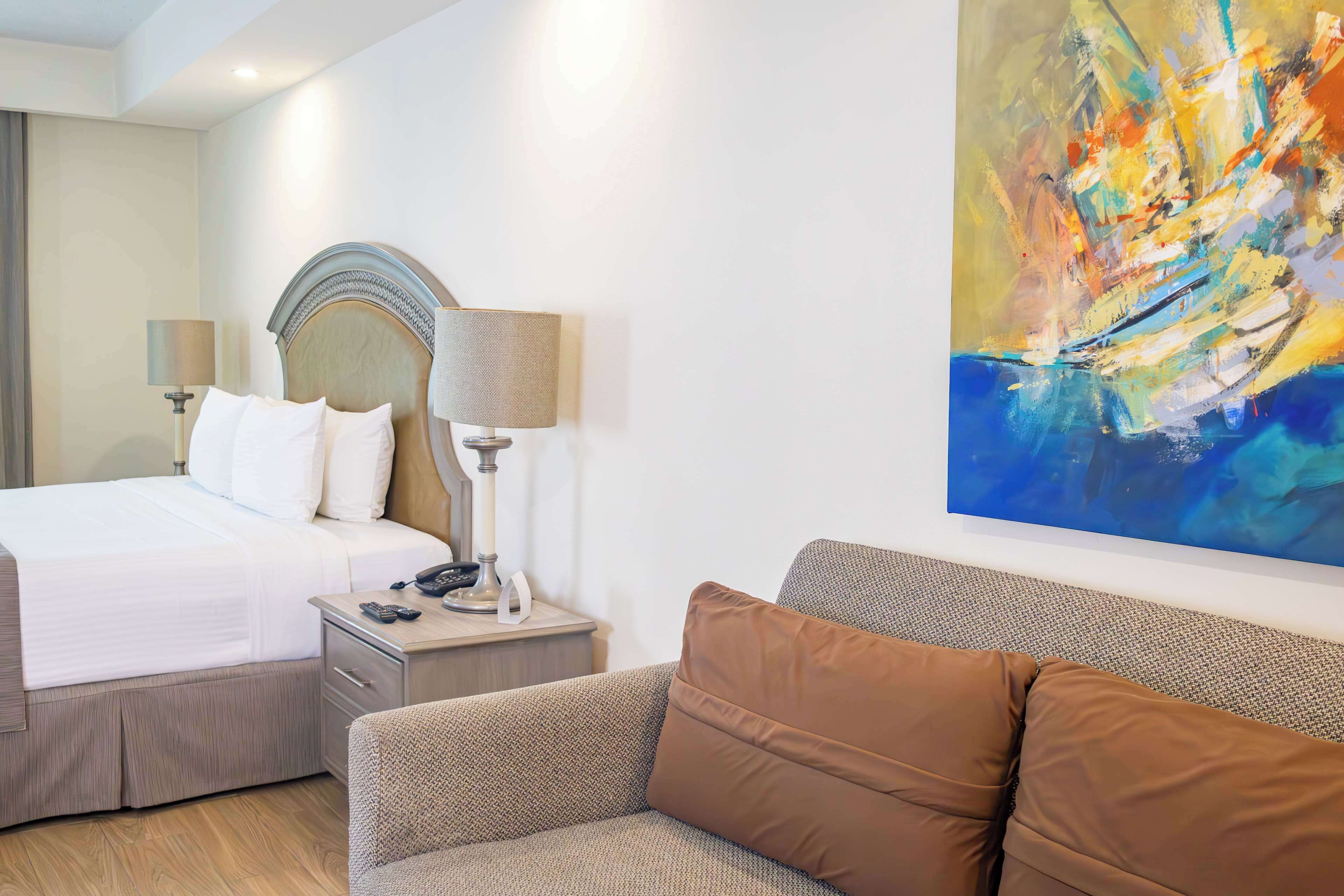Een hotelkamer met een bed, nachtkastje, lamp, schilderij en een bank.