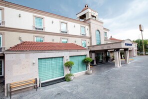 Un hotel con tejado de tejas rojas, un acceso cubierto y una torre del reloj.