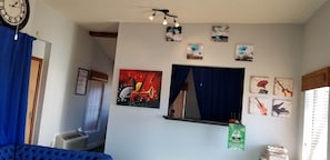 Una habitación con una cama, un reloj, una ventana con persianas, un aire acondicionado instalado en la pared y varias fotografías enmarcadas.
