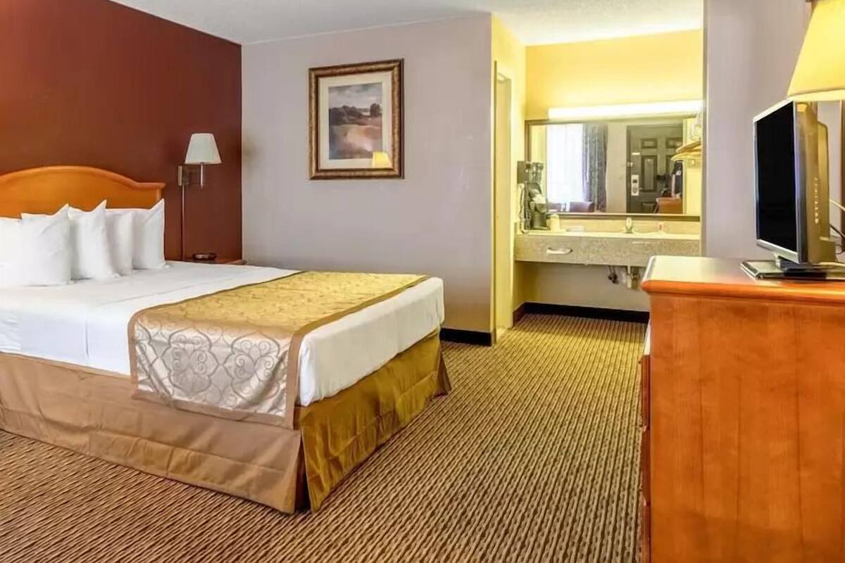 A hotel room with a bed, a bedside lamp, a mirror, a television, and a bathroom visible through an open door.