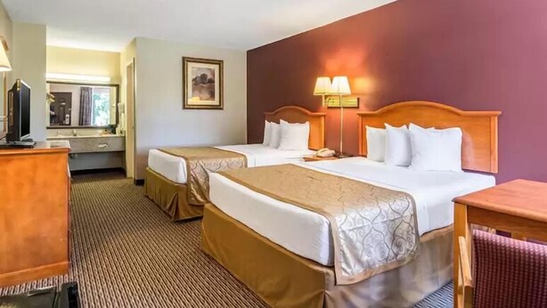 A hotel room with two beds, a desk, a chair, a lamp, and a framed picture on the wall. - The Parkwood Inn & Suites (Mountain View)